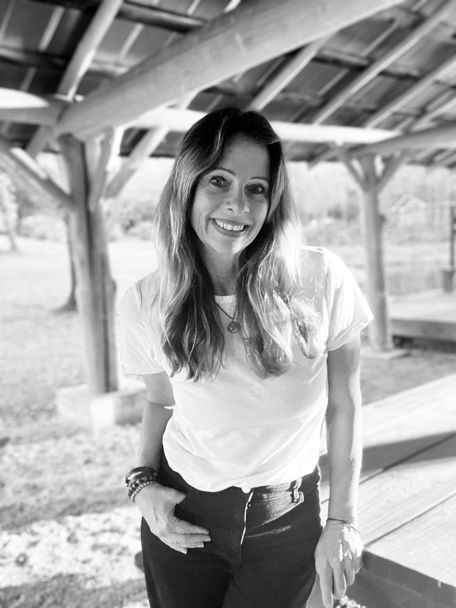 Person wearing a white t-shirt and dark pants standing under a wooden structure.