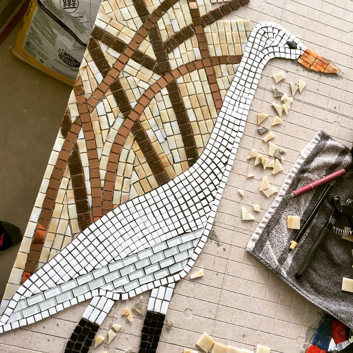 Mosaic goose art project on a table with tools and materials.