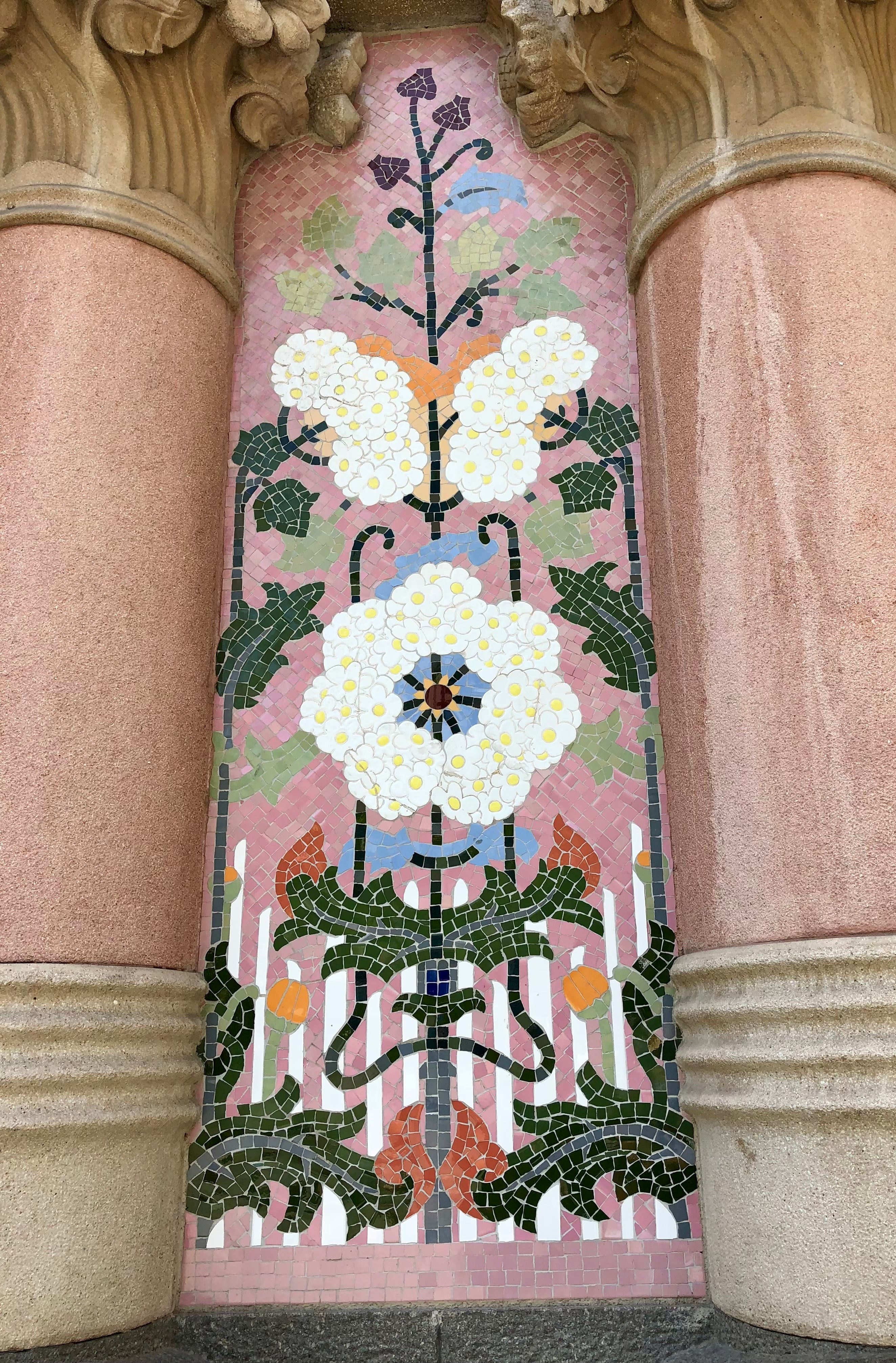 Decorative mosaic with floral patterns on a pink background between two columns.