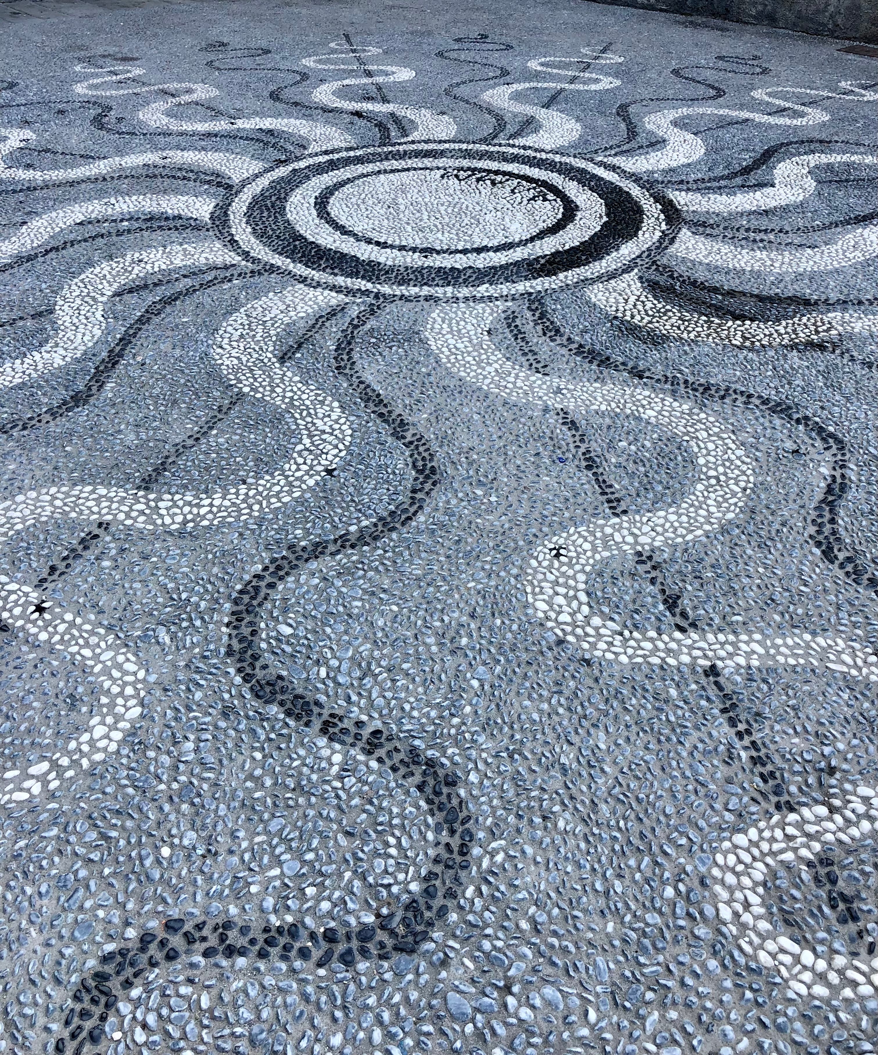 Mosaic pattern on a pavement with circular and wavy designs.