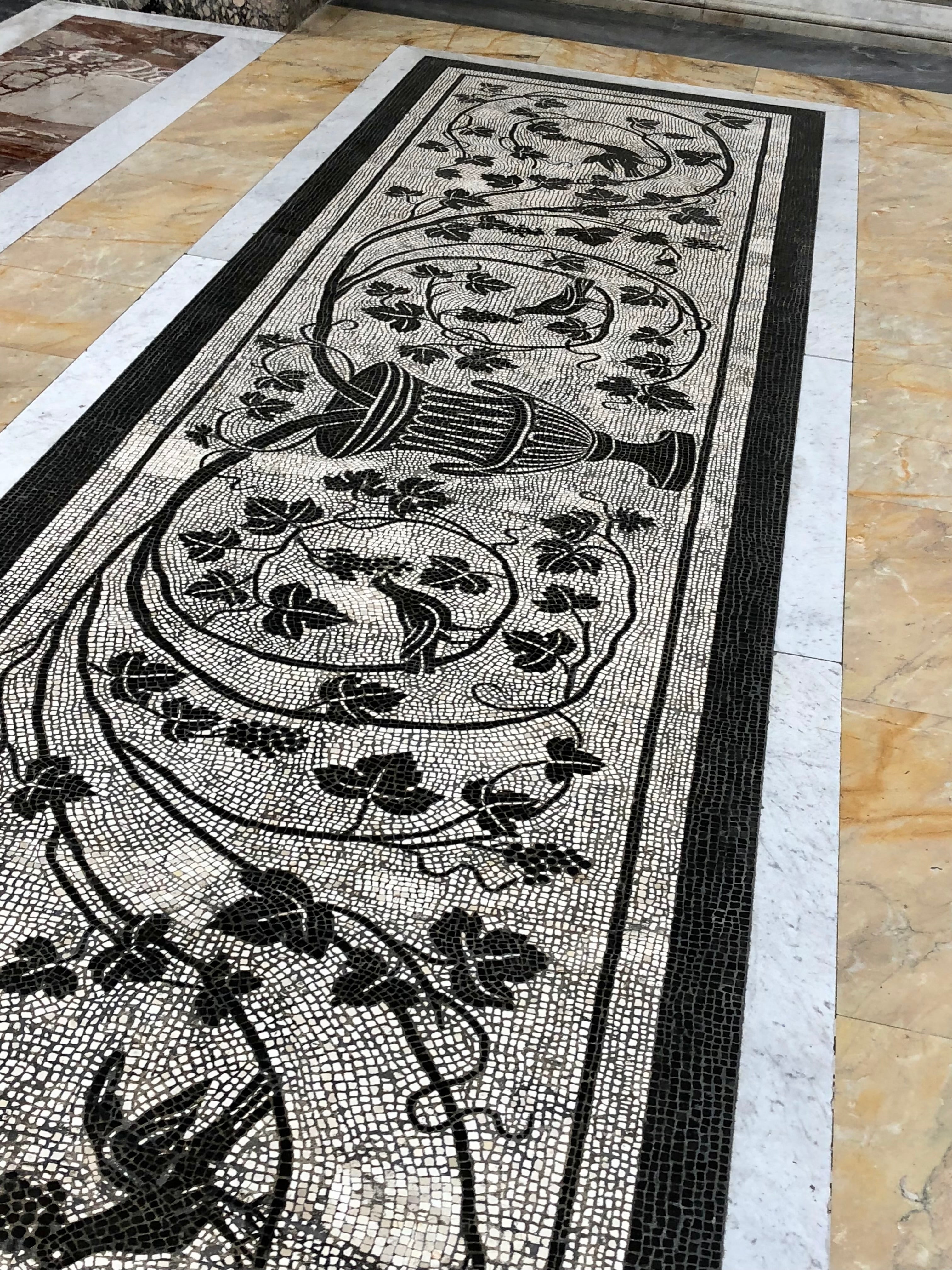 Mosaic design with floral patterns and a vase on a stone floor.