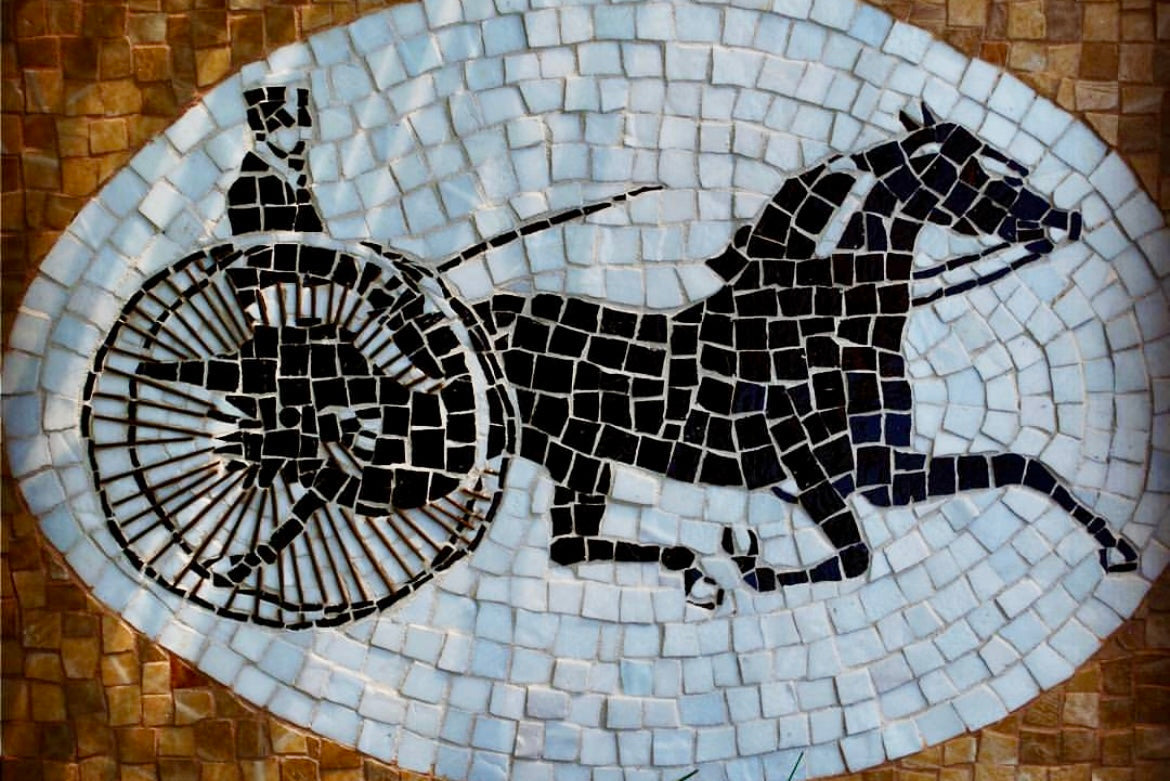 Mosaic artwork of a horse pulling a cart on a stone floor.