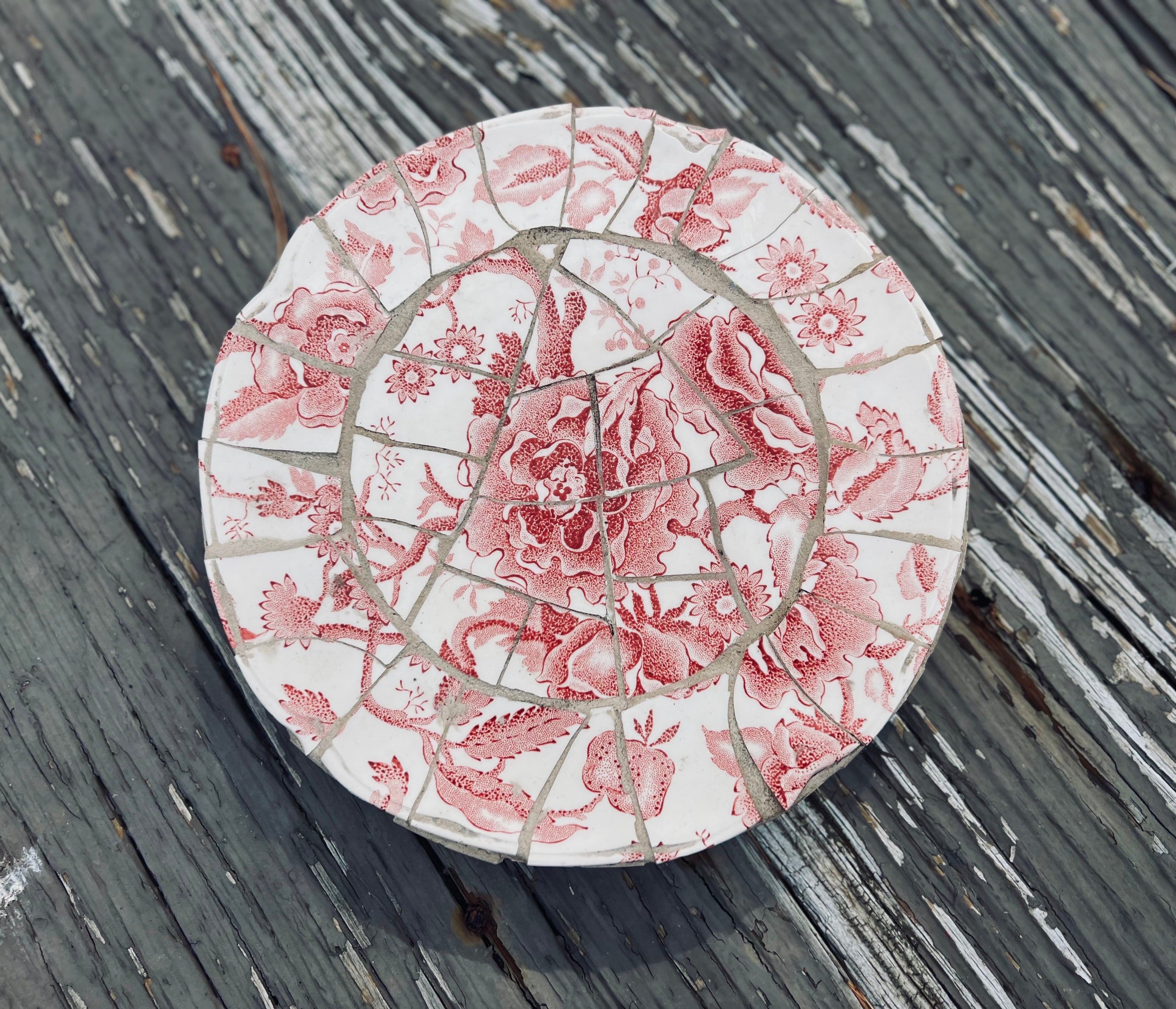 Mosaic art piece with pink floral design on a wooden surface