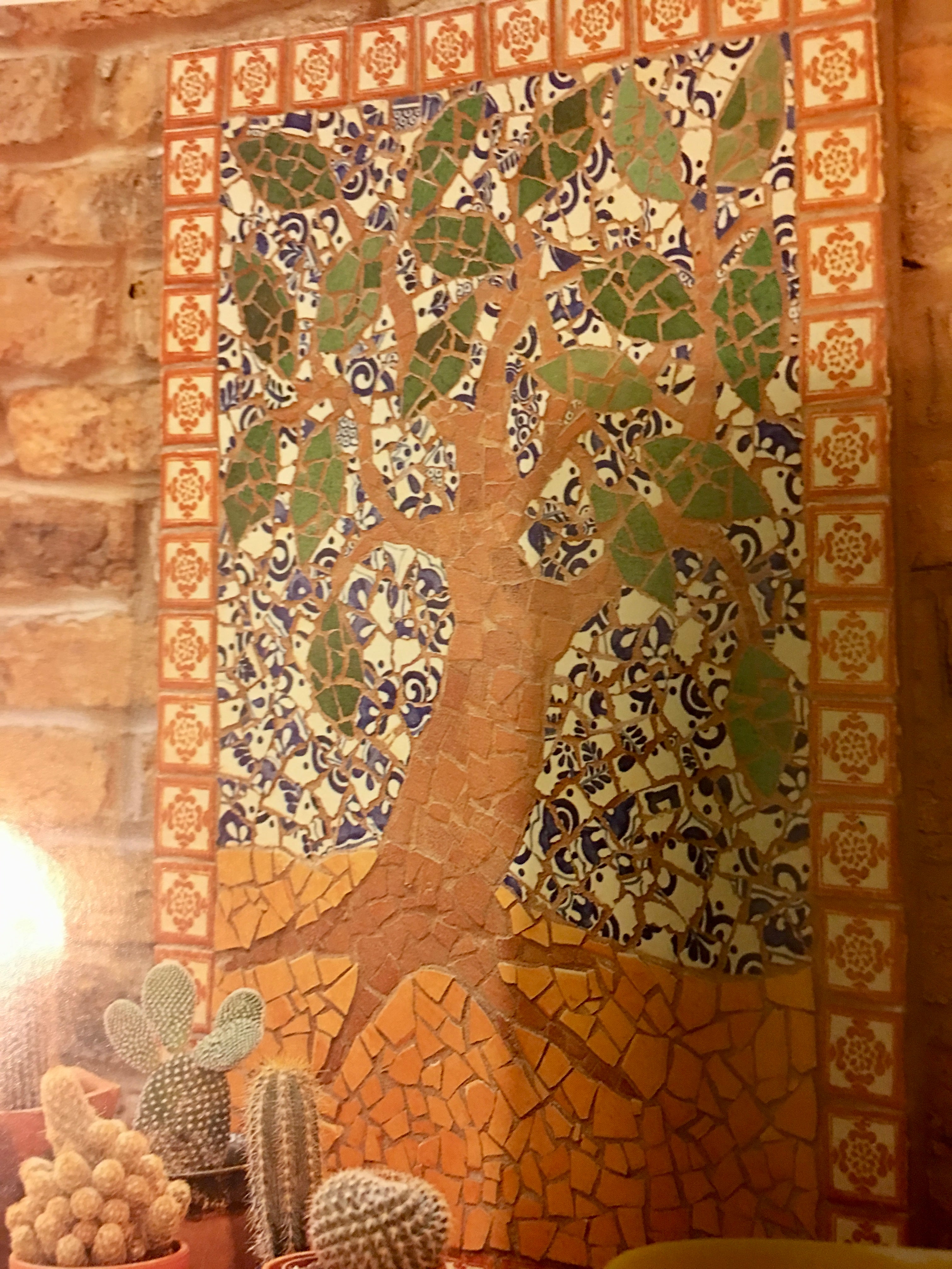 Mosaic wall art of a tree with animals on a brick wall