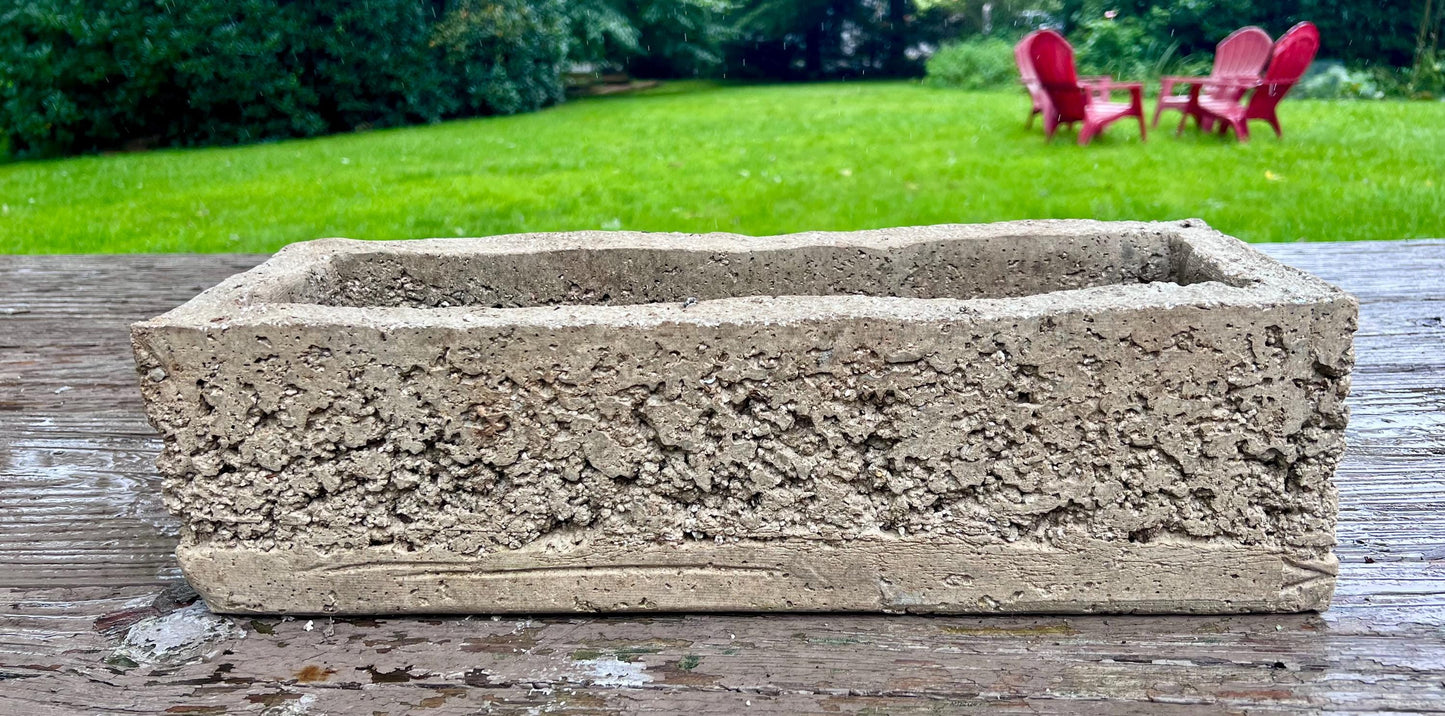 Rectangular concrete planter on a wooden surface with a garden in the background