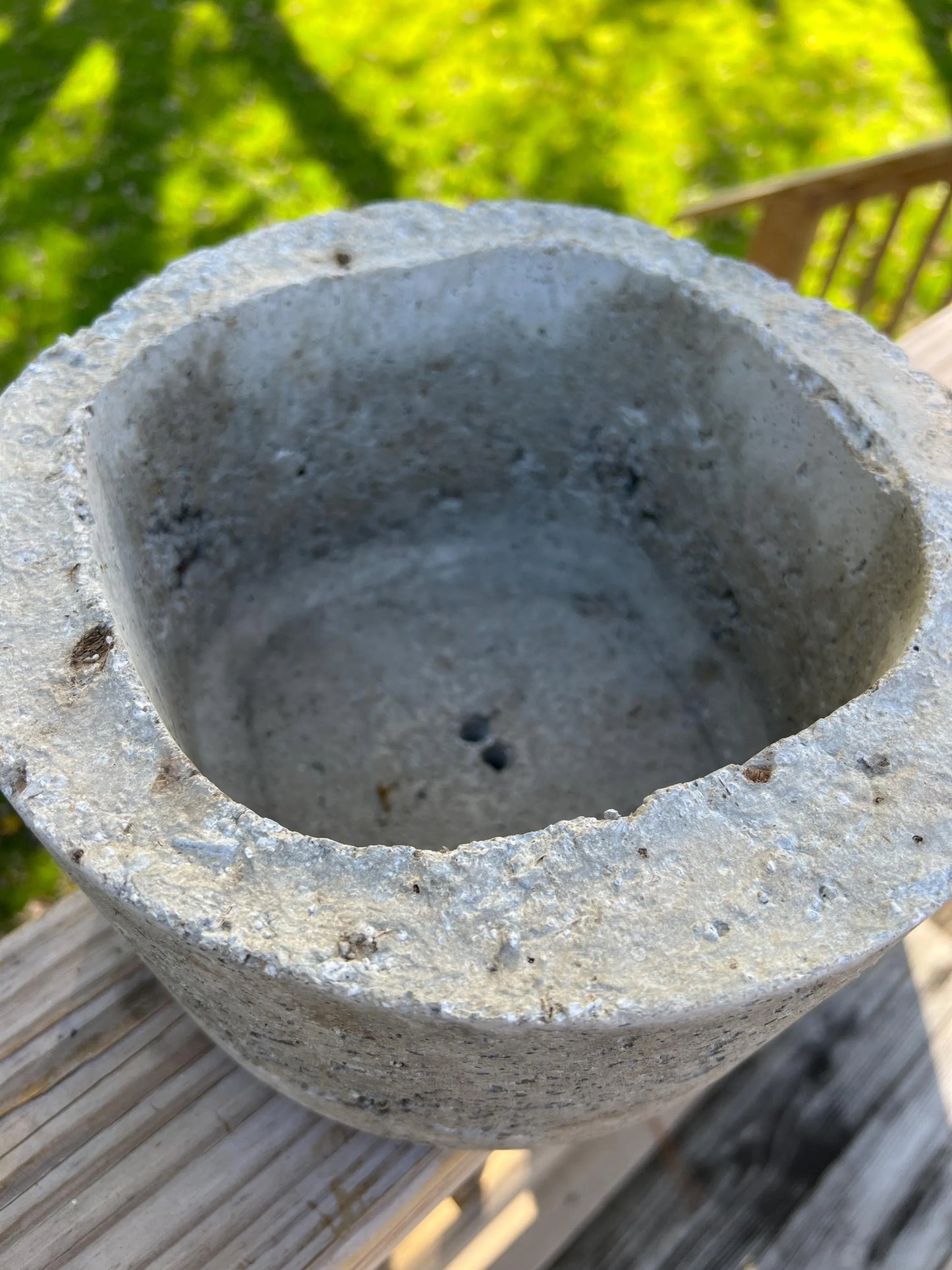 Concrete bowl on a wooden surface with a blurred green background