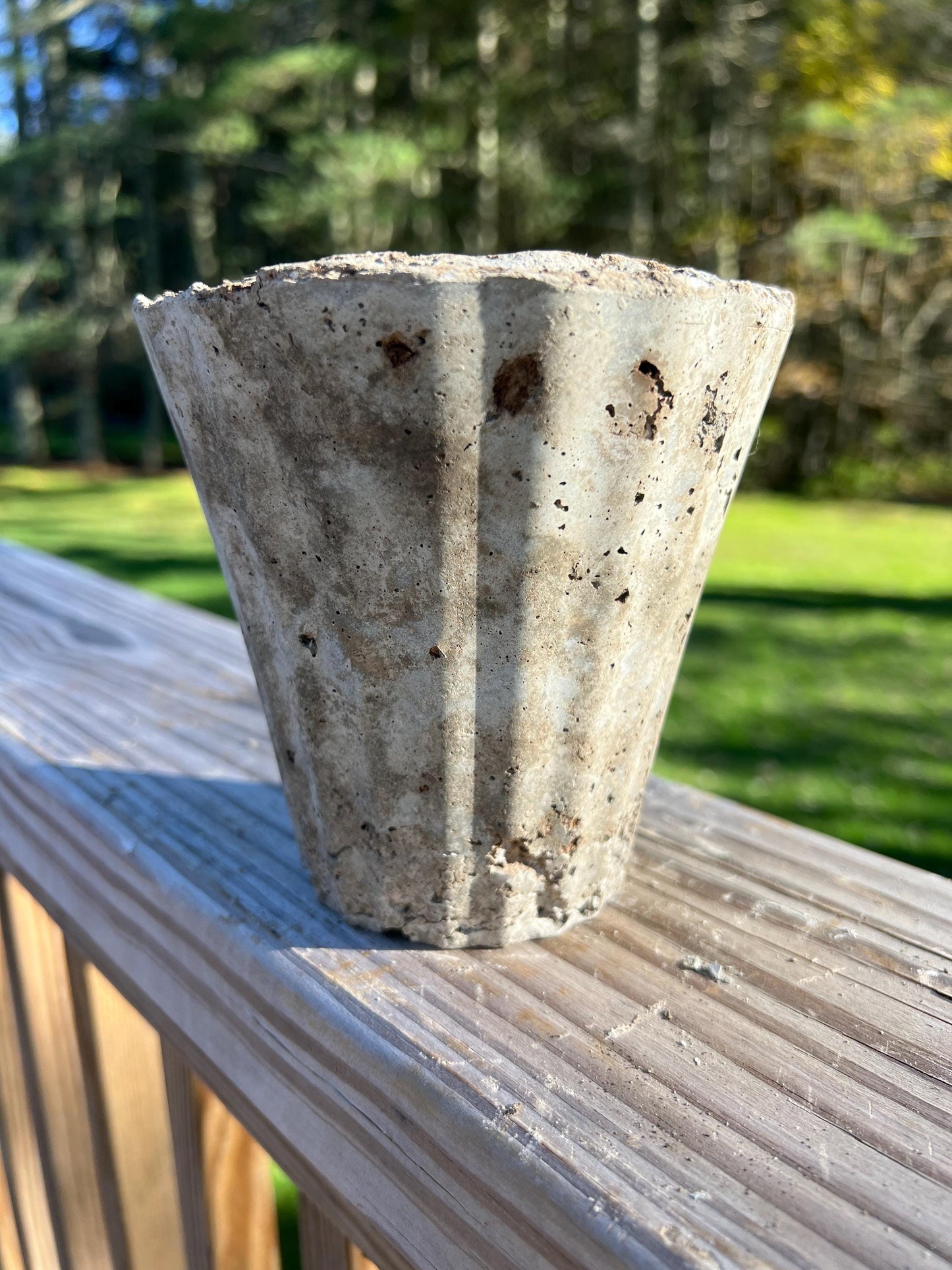 Concrete flower pot on a wooden deck with a blurred green outdoor background