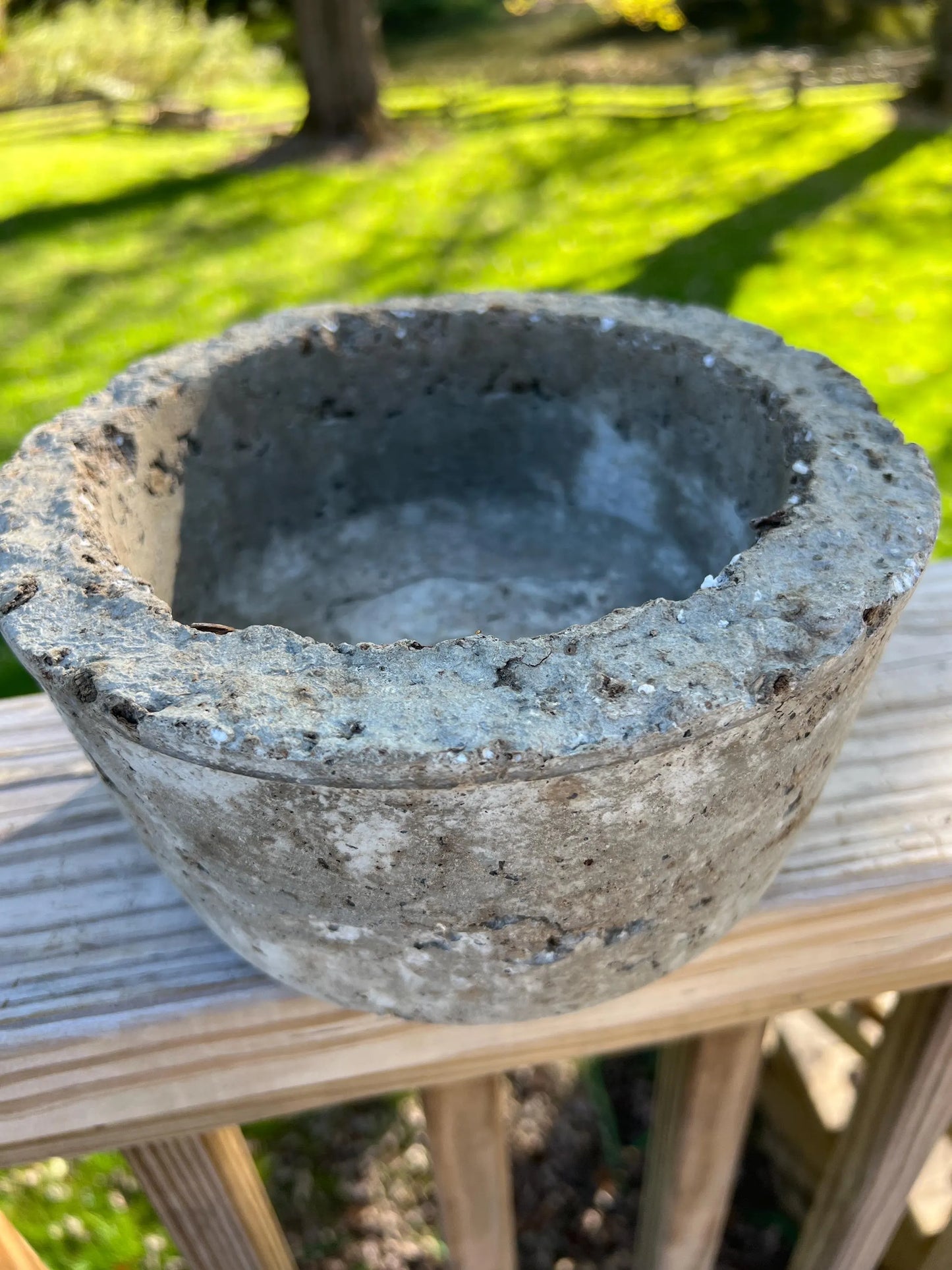 Concrete planter on a wooden surface with grass and a tree in the background