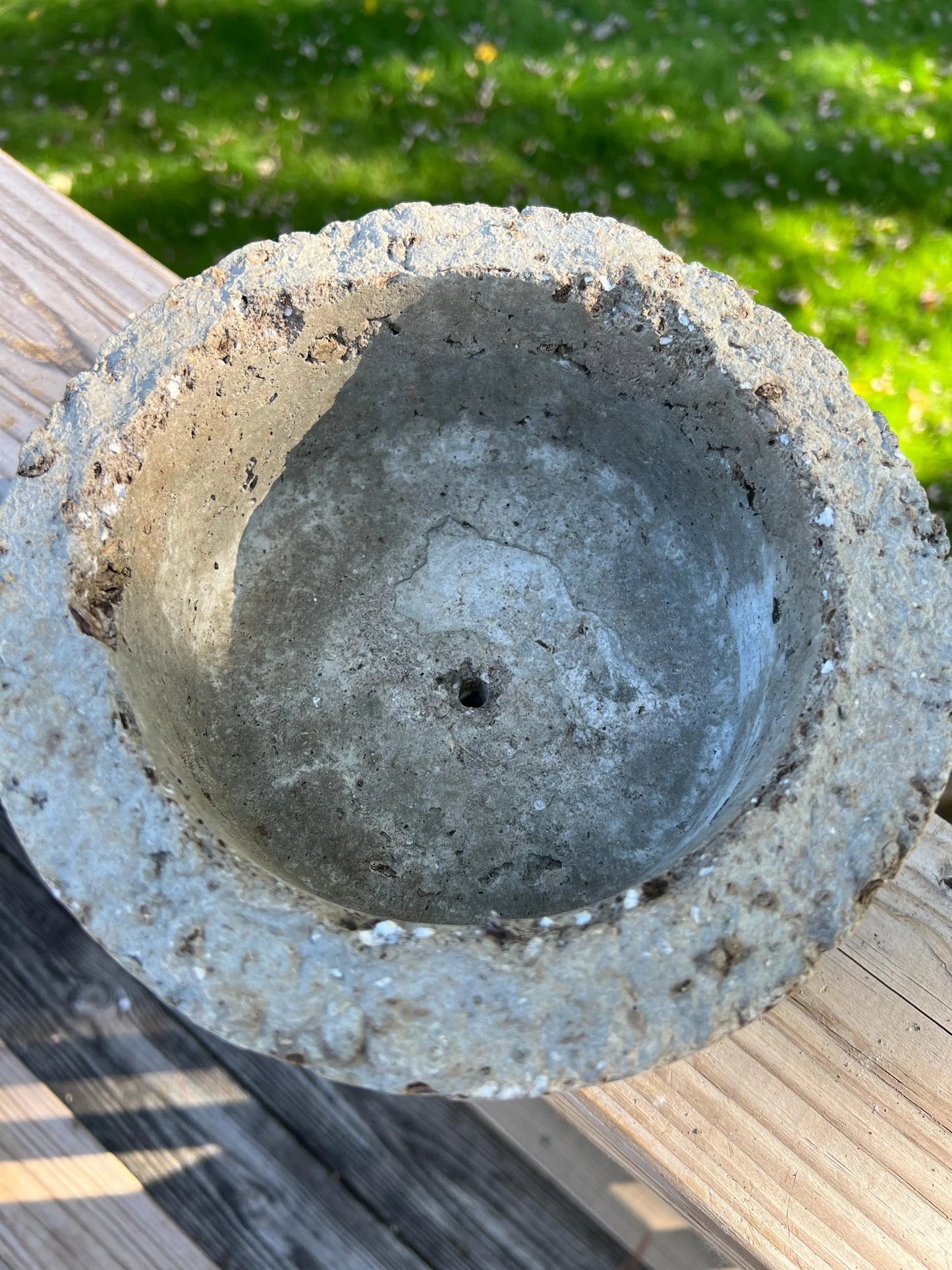 Concrete flower pot on a wooden surface with grass in the background