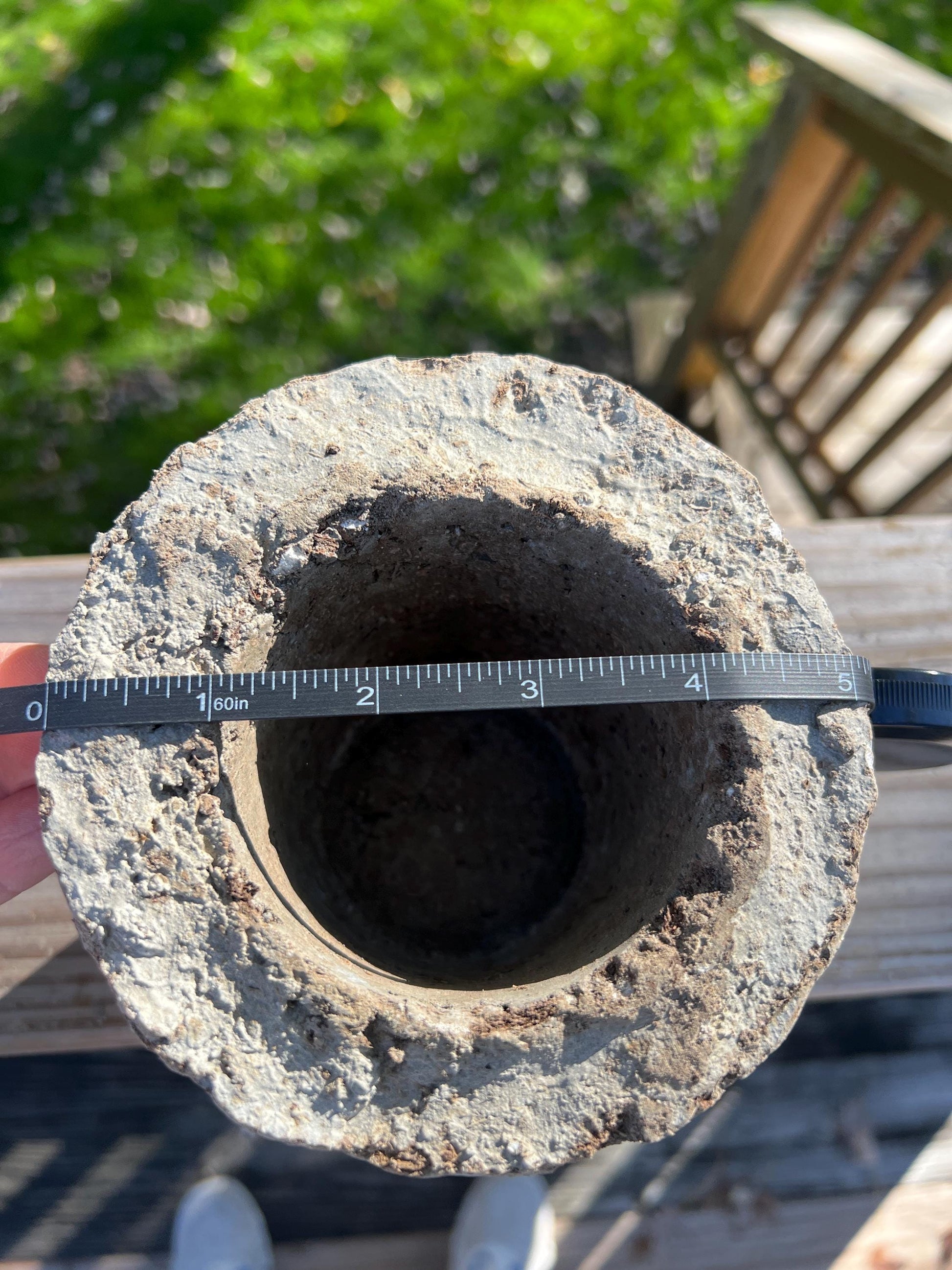 Cylindrical stone object with a measuring tape around it, outdoors.
